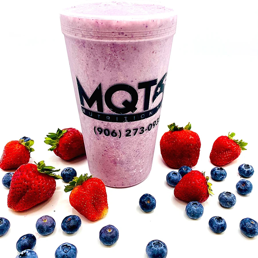 Pink smoothie in a cup with strawberries and blueberries.