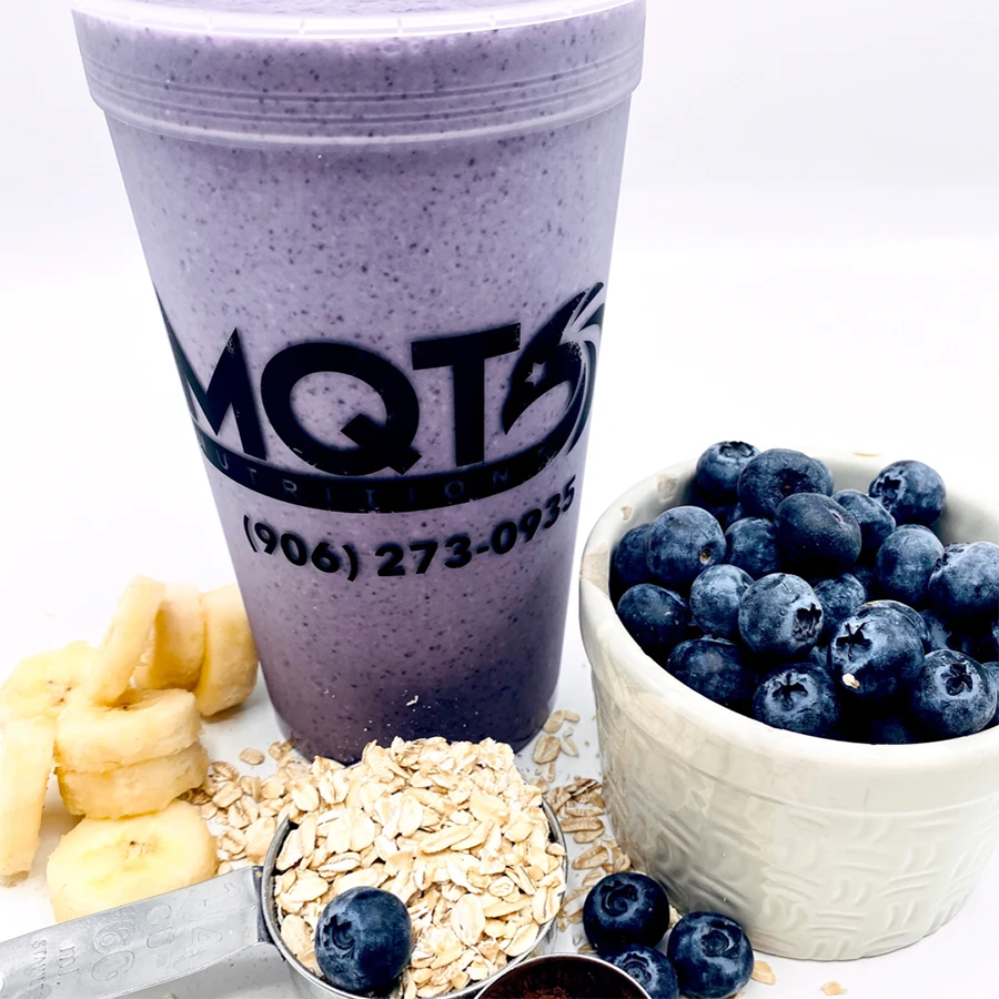 Purple smoothie in a cup, surrounded by blueberries, bananas, and oats.