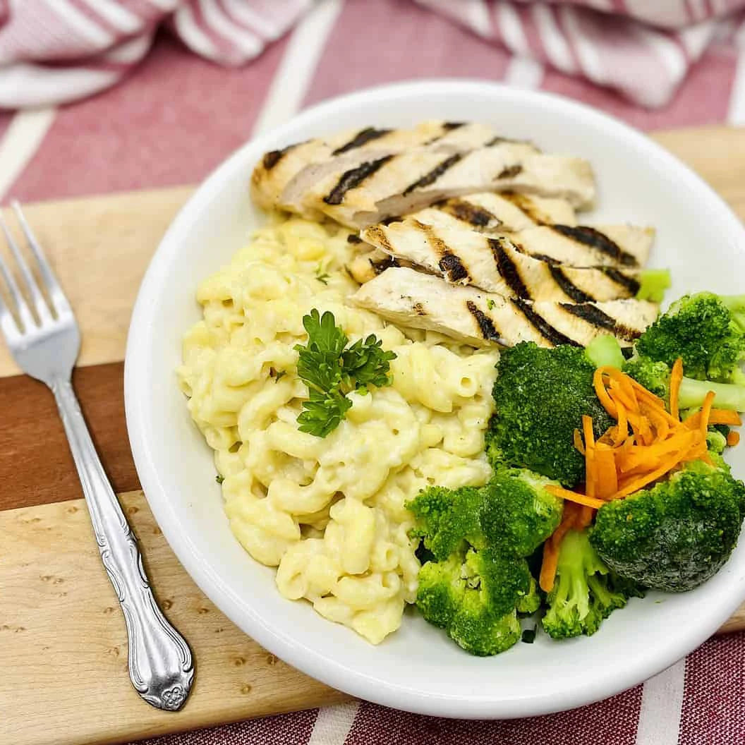 Grilled chicken alfredo and broccoli on a wooden cutting board.