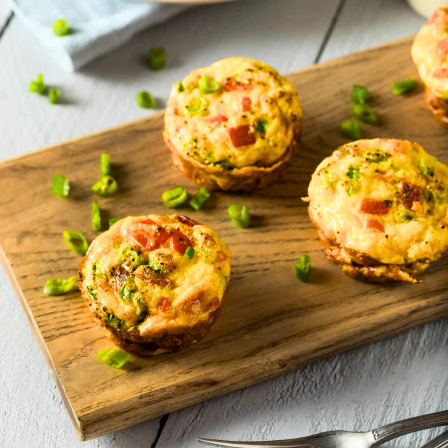Three egg muffins on a wooden board with green peas scattered around