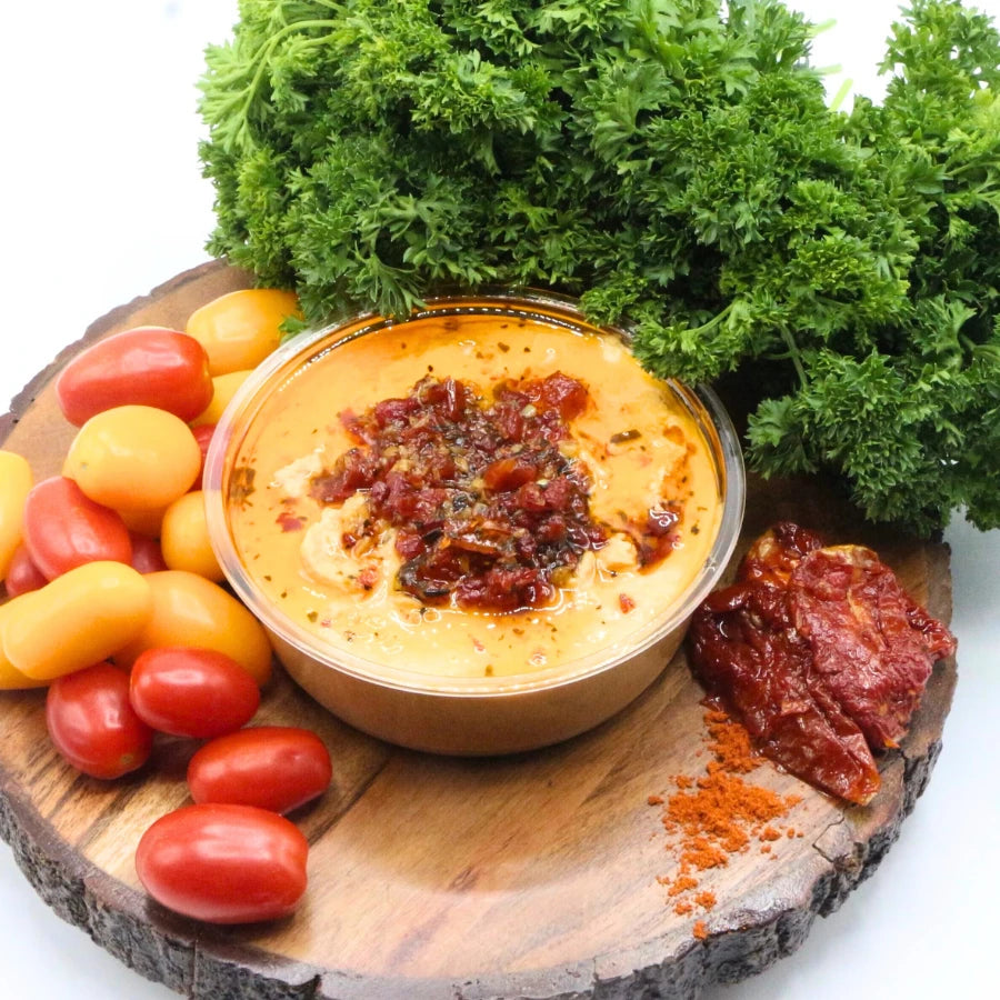 Dip in a glass bowl with sun-dried tomatoes on a wooden board with cherry tomatoes and parsley.