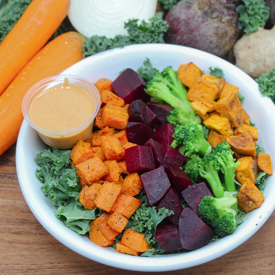 Assorted vegetables including carrots, broccoli, and beets in a bowl with a side of dipping sauce.