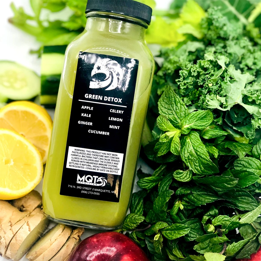 Green detox juice bottle with ingredients on greens