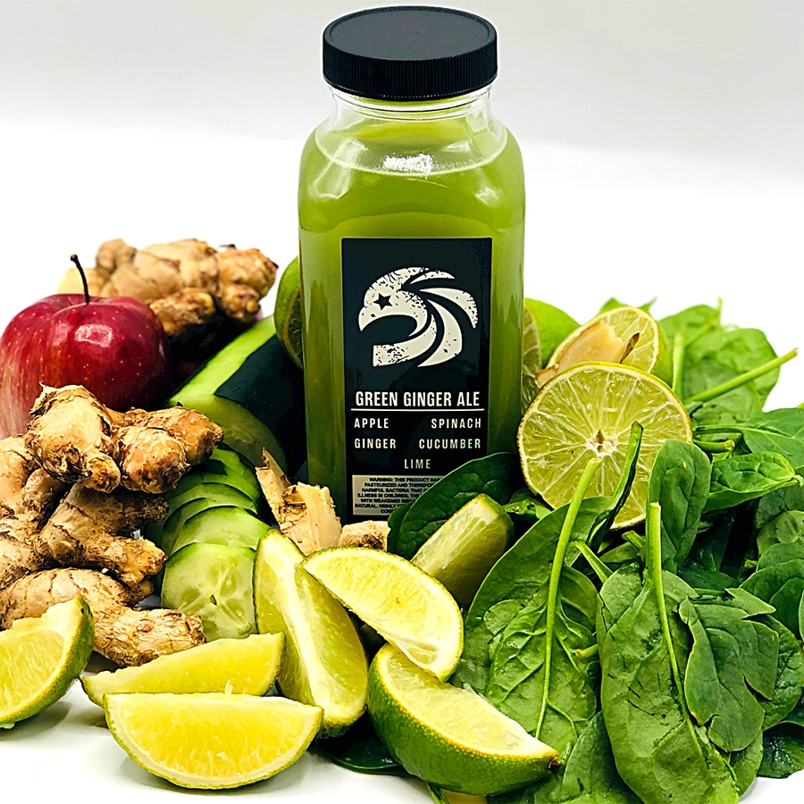 Bottle of green ginger ale surrounded by fresh ingredients like apples, limes, and spinach