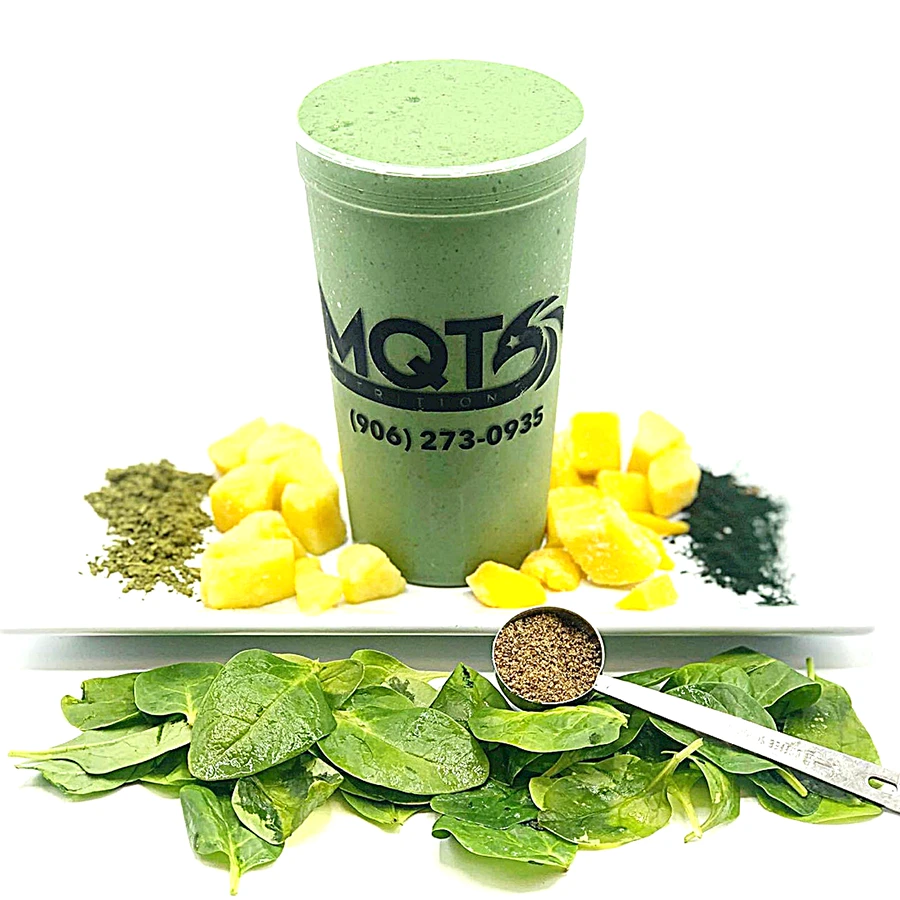 Green smoothie in a cup with ingredients like spinach, pineapple, and a scoop of protein powder.