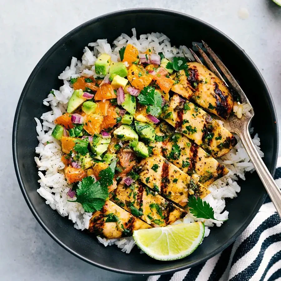 Grilled chicken with avocado salsa on a bed of rice in a black bowl.