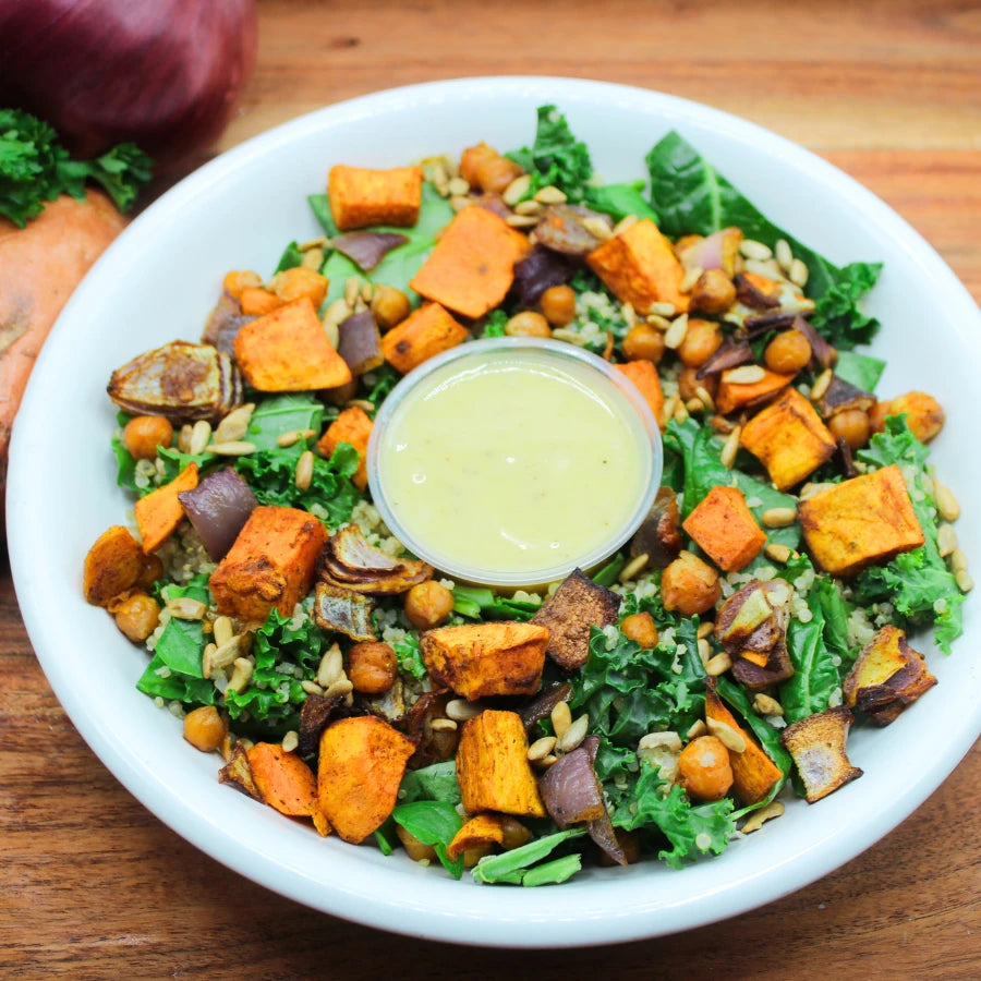 Salad with sweet potatoes, kale, and chickpeas in a white bowl on a wooden surface.