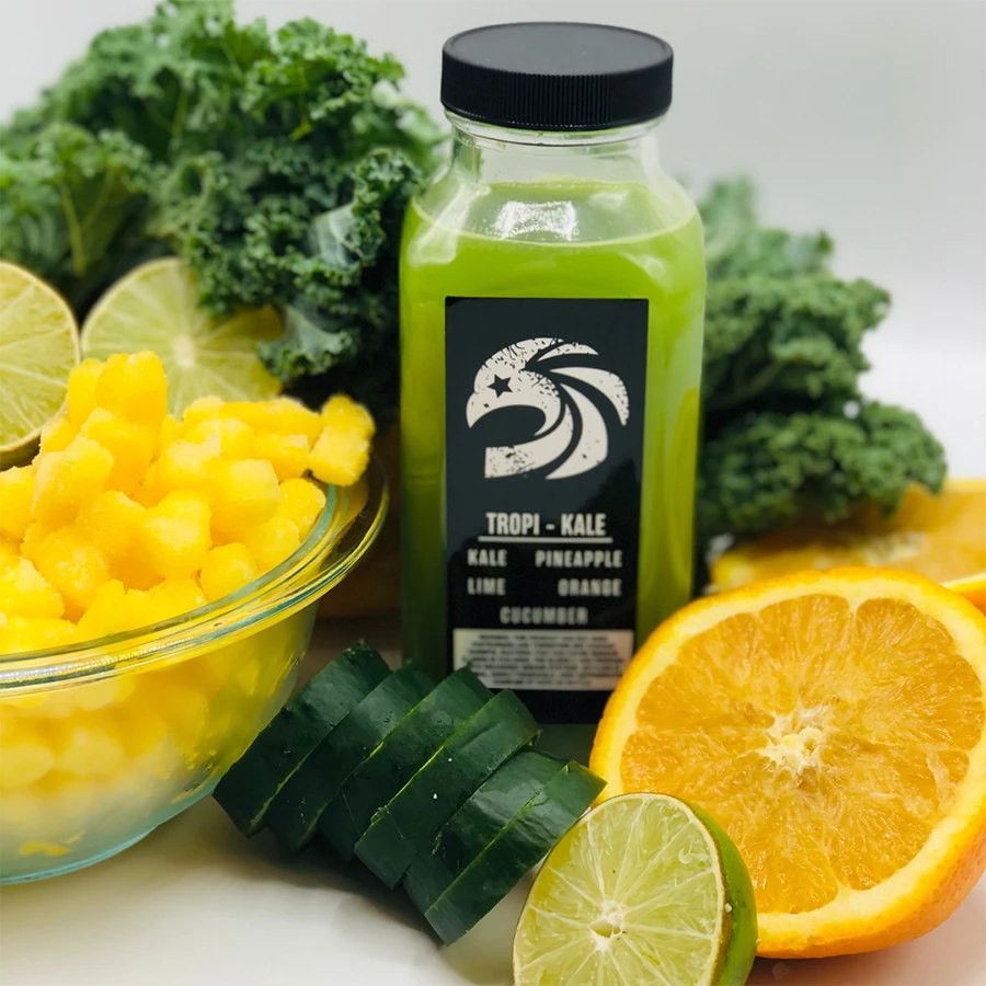 Green juice bottle labeled 'Tropi-Kale' surrounded by kale, oranges, and other fruits