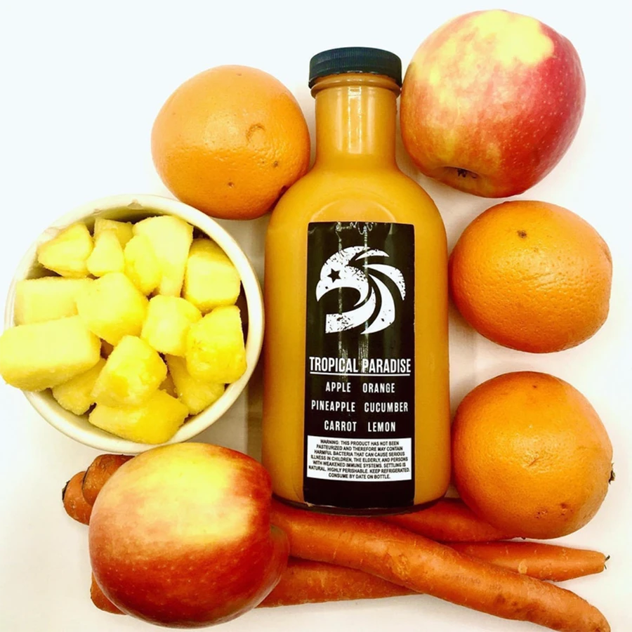 Bottle of 'Tropical Paradise' juice surrounded by fruits and vegetables.