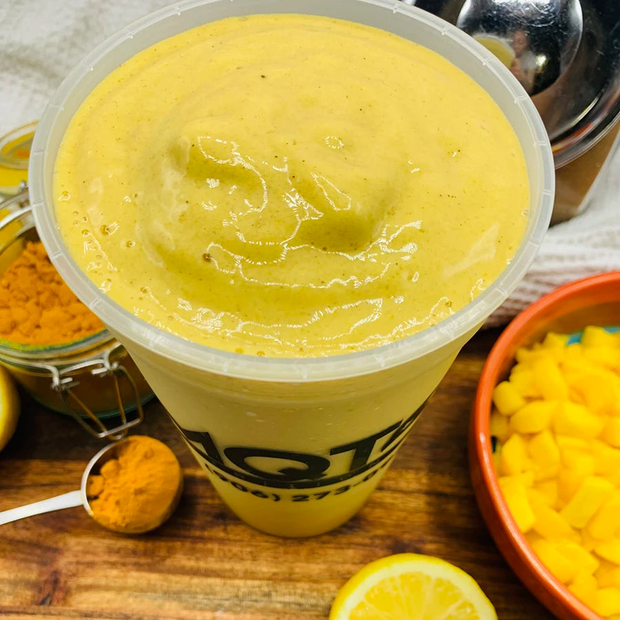 turmeric smoothie in a cup with turmeric and lemon on a wooden surface